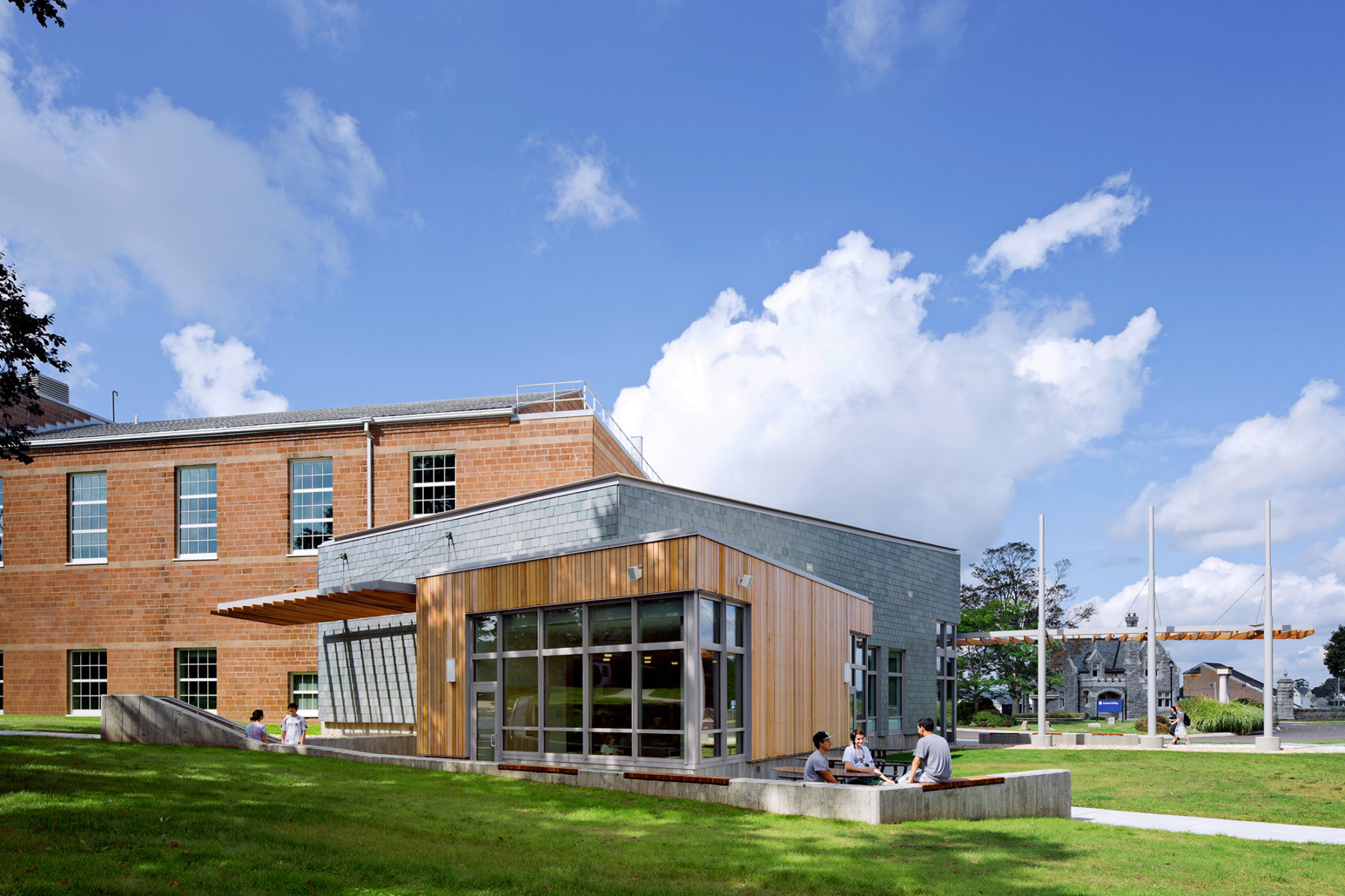 Exterior photo of building. Students sit in groups on the building's plaza