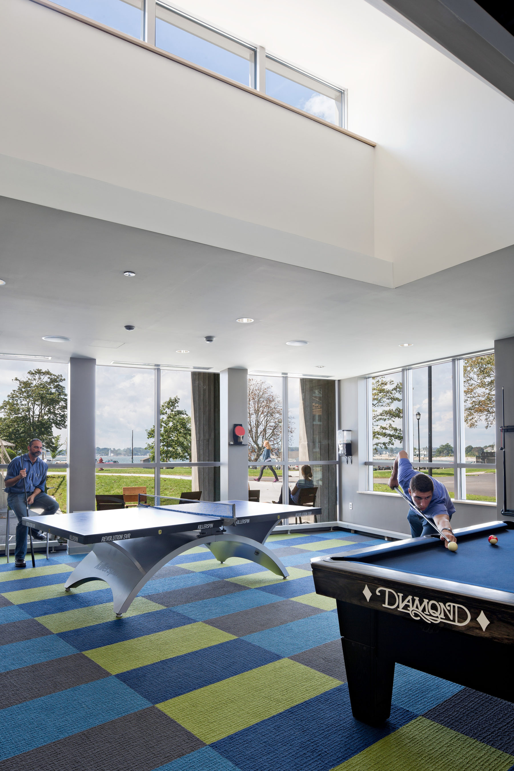 Interior photo of pool and pingpong table. Young man is setting up his pool shot.