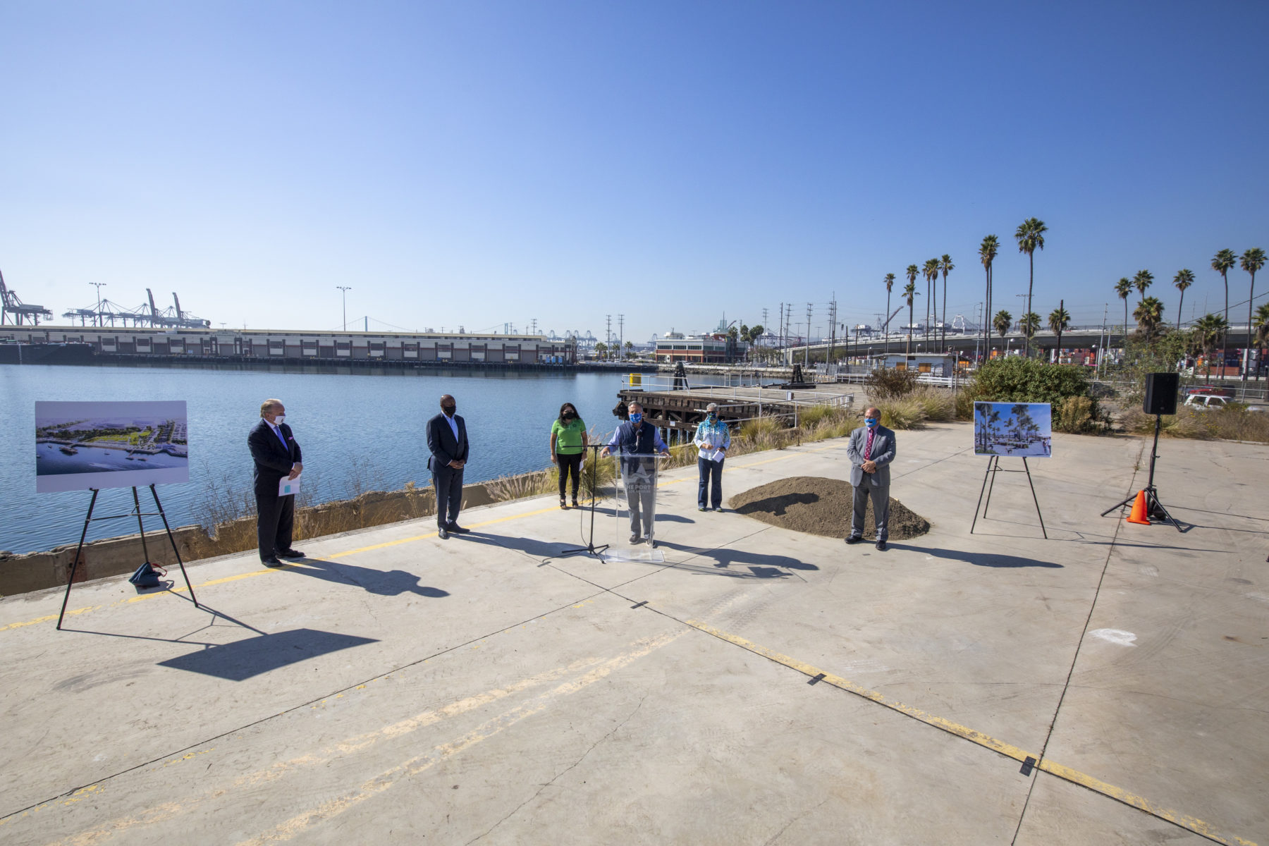 People standing, socially distanced, around a podium in front of the port