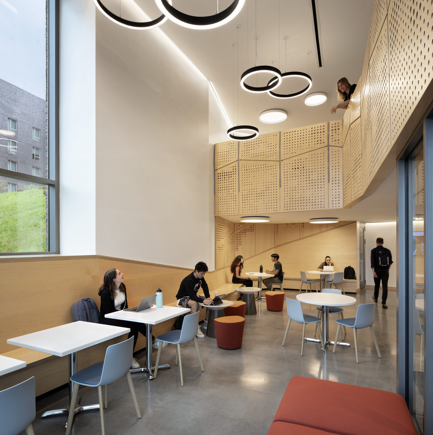 interior photo of building entry. students sit at tables in a double height space.
