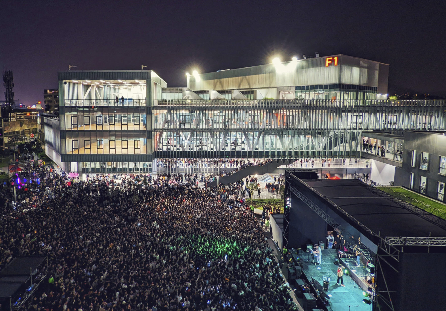 exterior photo of building at night. the lights illuminate the building showing the structure. on the right a stage is set up on the plaza and the plaza itself is covered with people