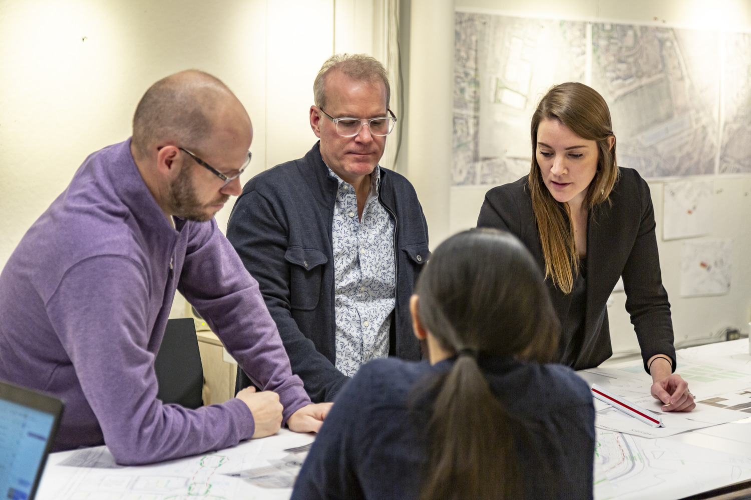 Four people standing around a table looking at a drawing together. Emily, the author is on the right speaking