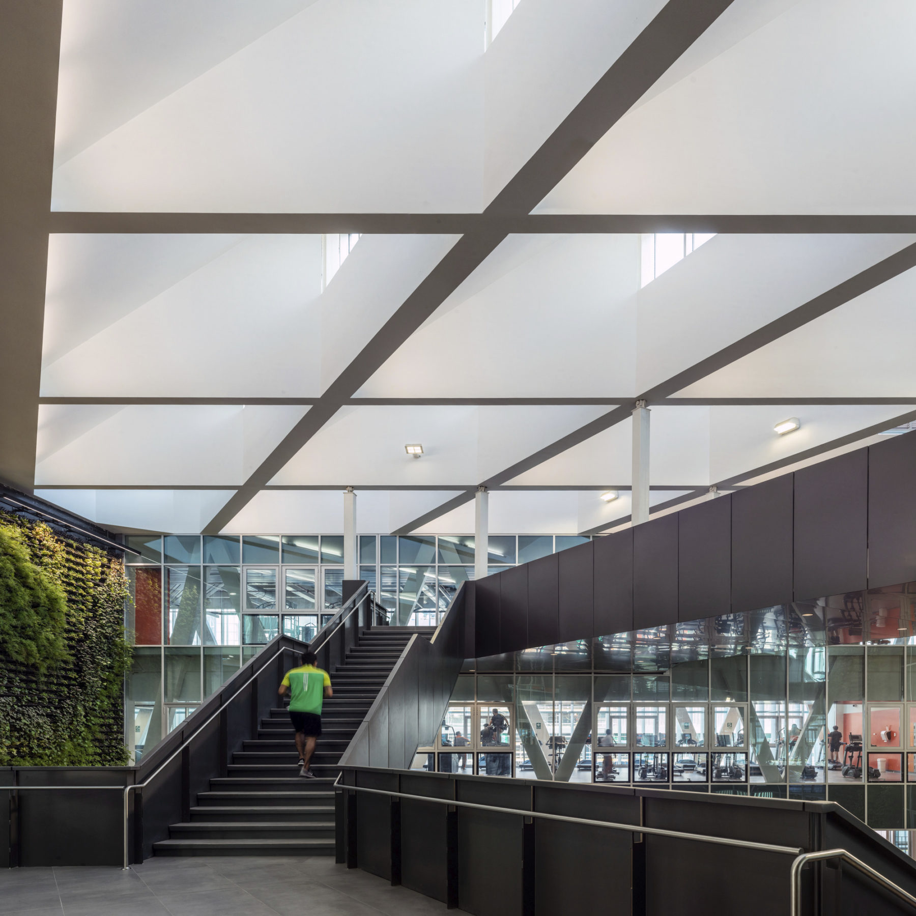 interior photo of bridge connection. a single student climbs the stairs with a large grid of skylights above.