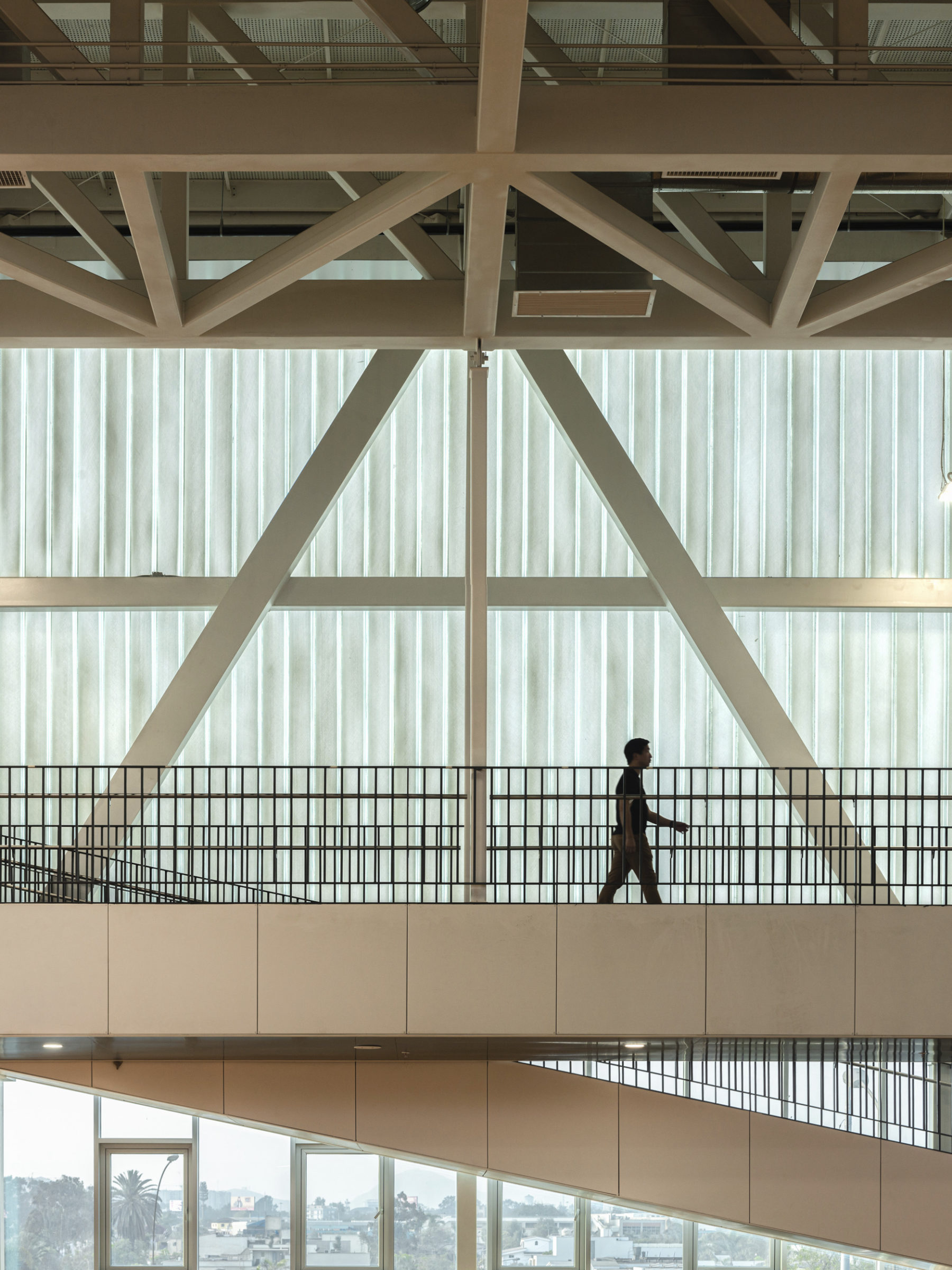 interior photo of a singular student walking on elevated bridge; structural trusses visible in the background