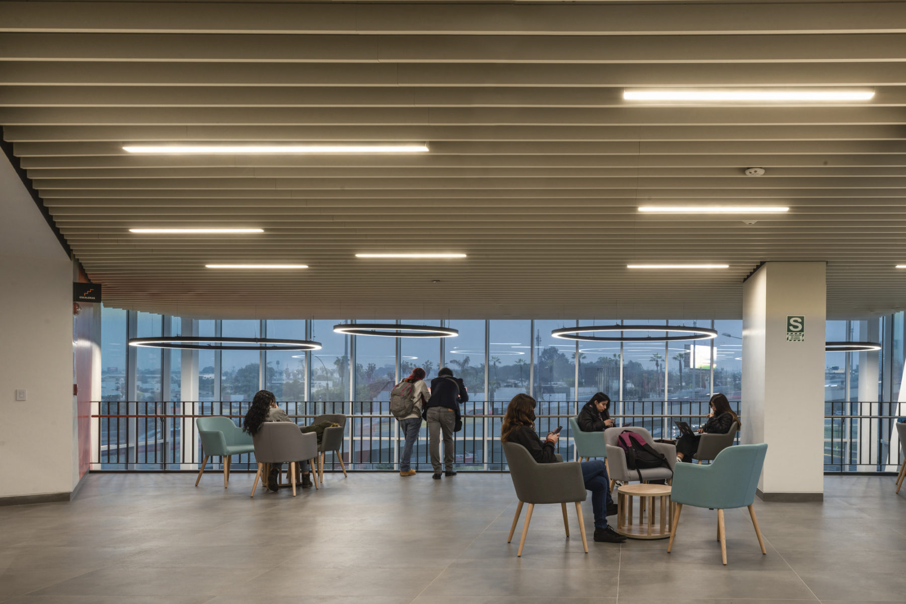interior photo of student overlook area with students sitting in soft seating,, illuminated by lights embedded in a wood slat ceiling