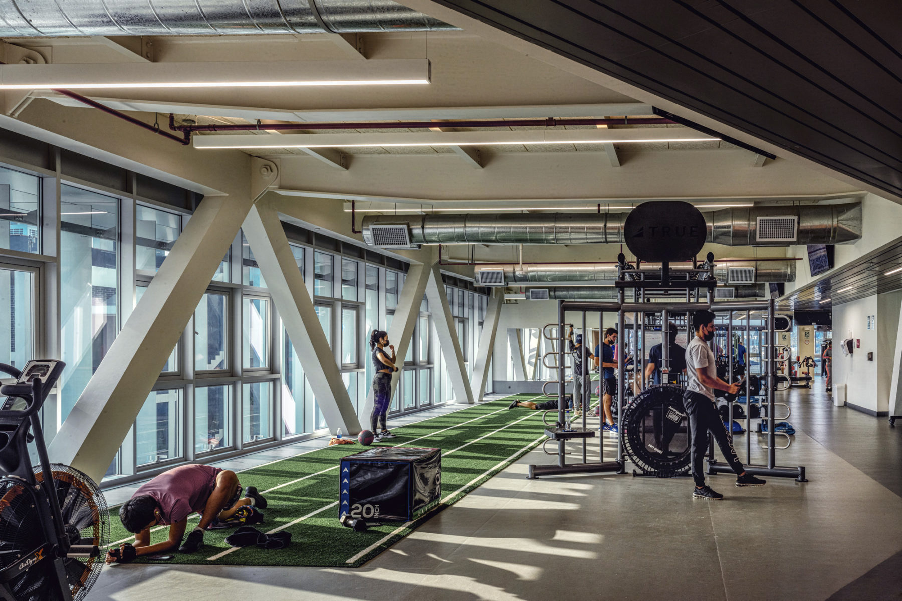 interior photo of crossfit area with a single student working out on a green carpet near the exterior building trusses