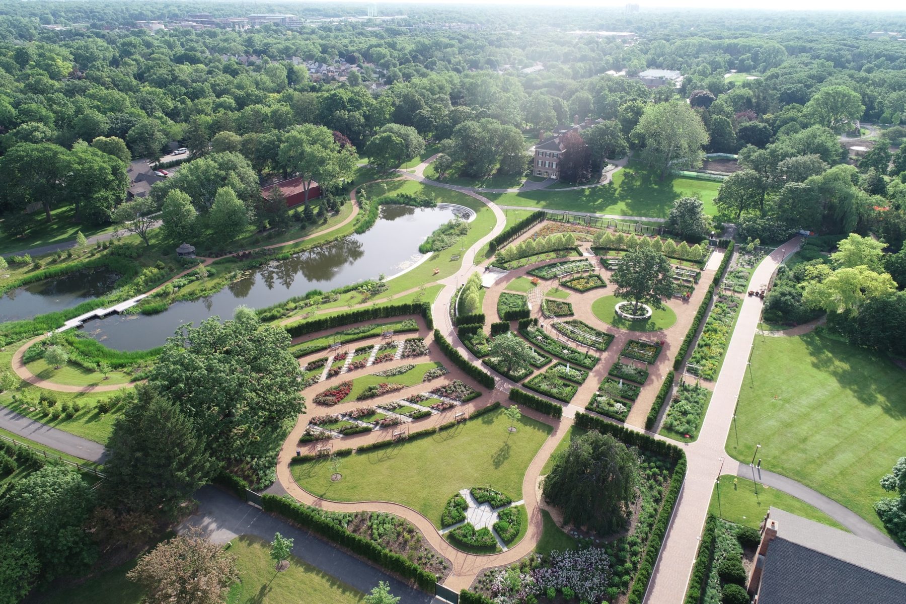 aerial view of park: colorful manicured parks, green lawns, pathways, a body of water, and a large patch of trees