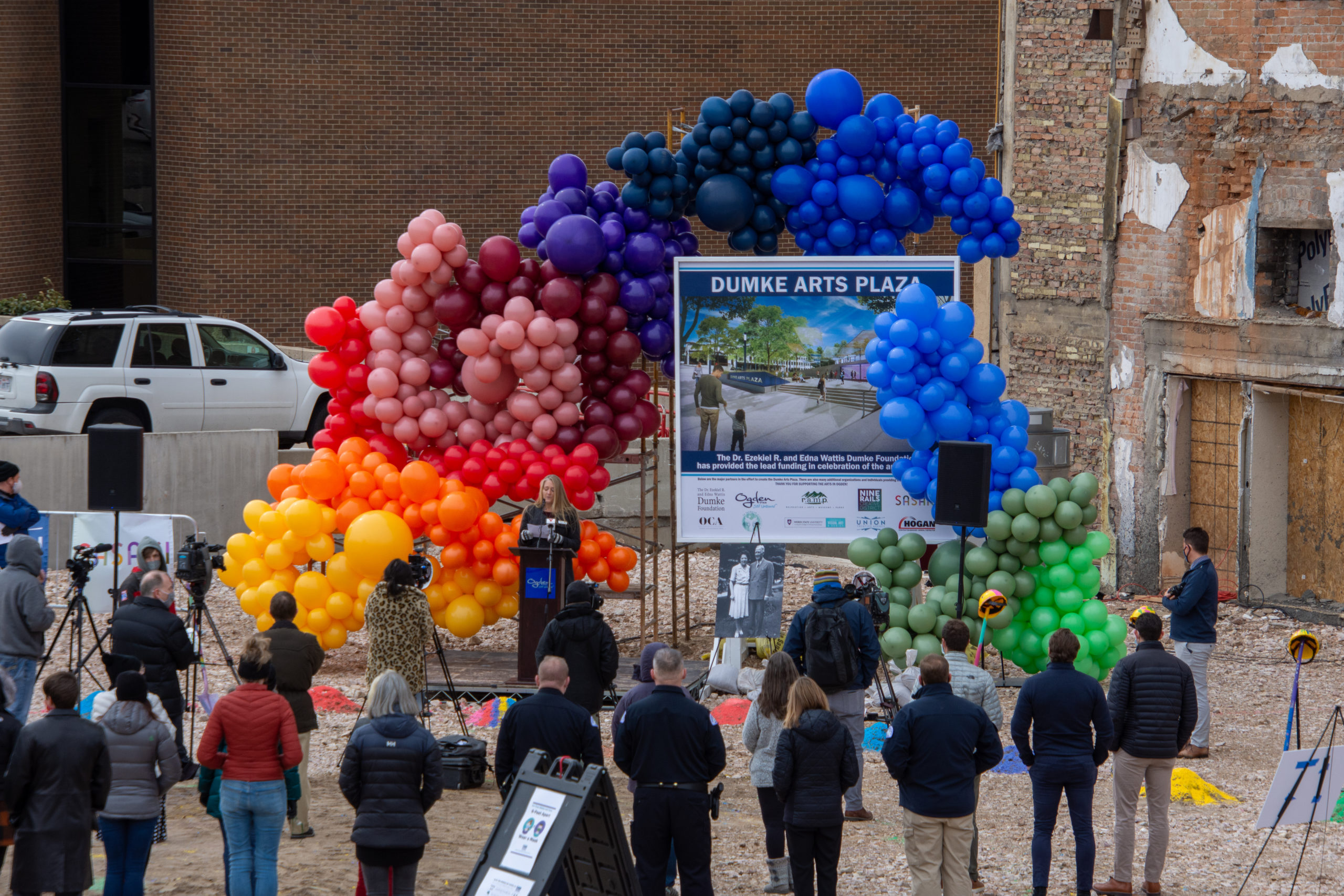 People socially distant at outdoor groundbreaking event with lots of rainbow balloons