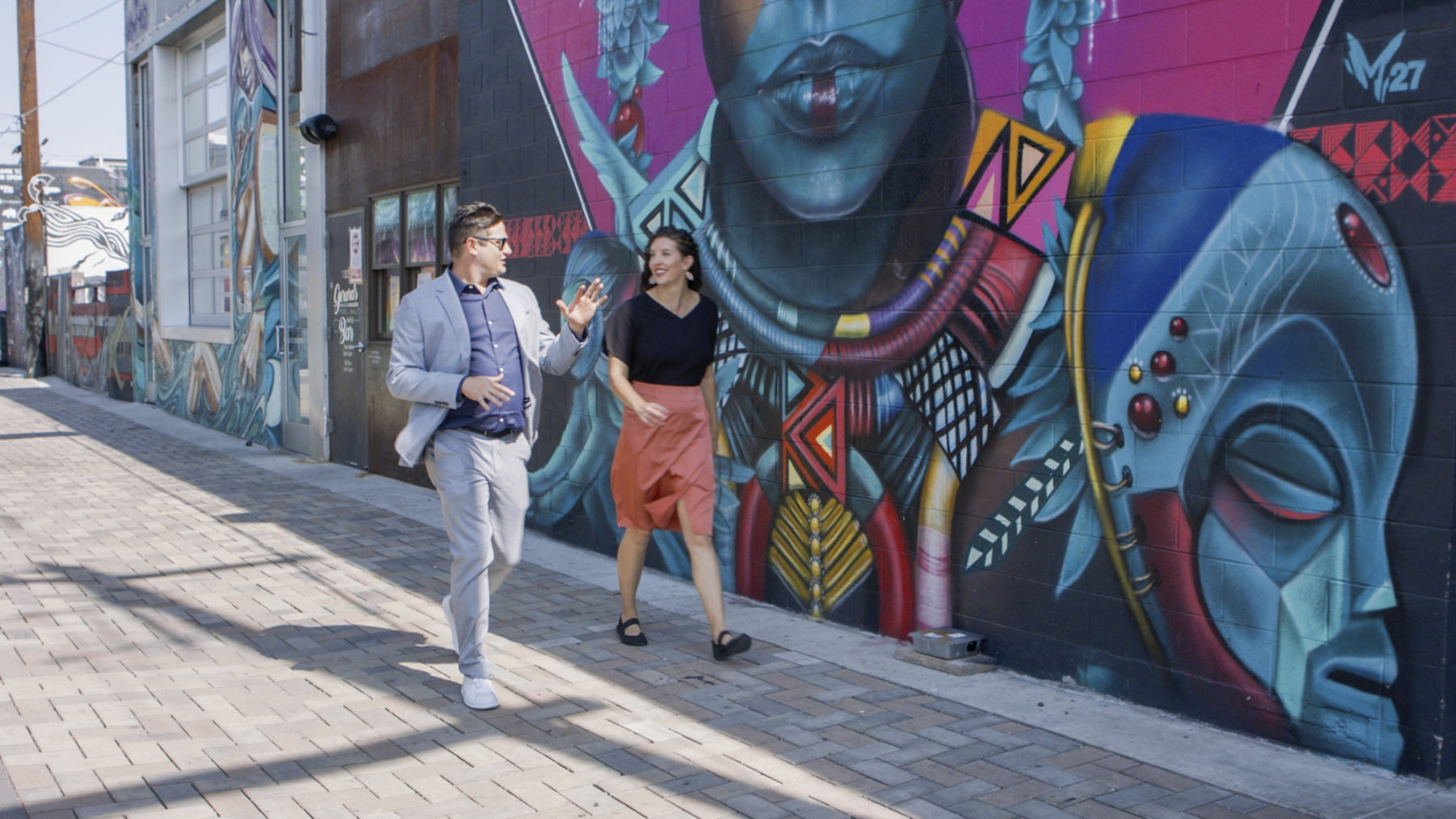 two people walk down a street in front of large art murals