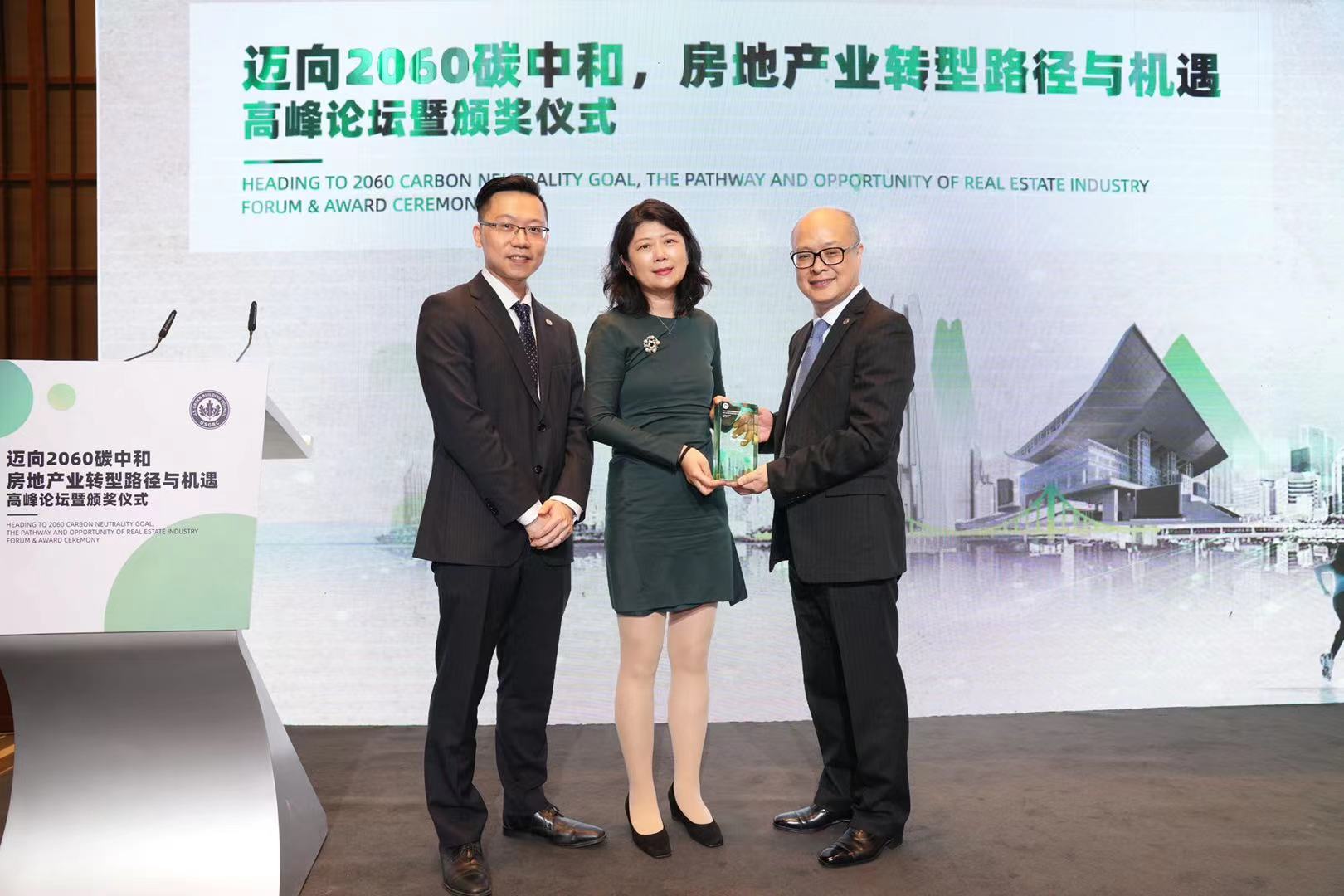 Dou Zhang stands in between two men on stage while accepting her award