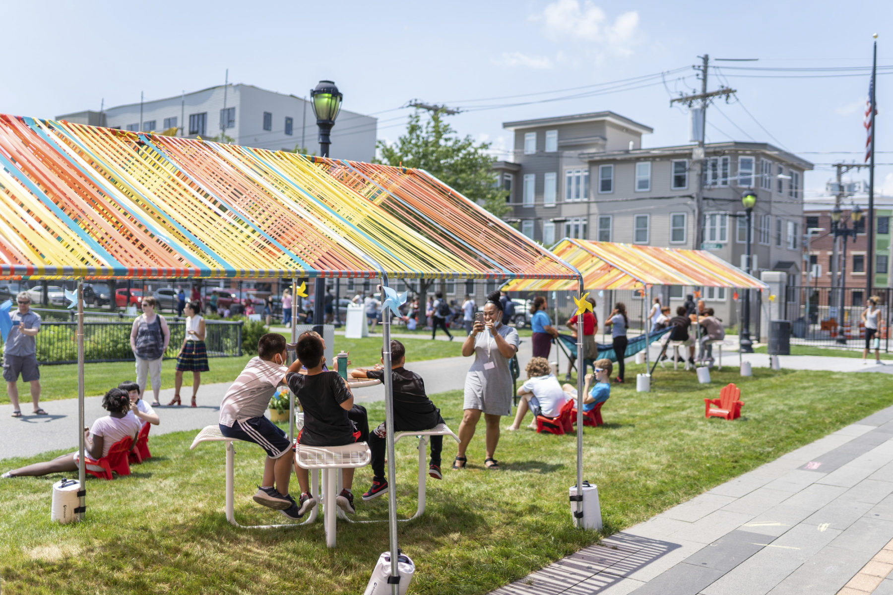 Someone takes a picture of a group of children under a colorful shade structure equipped with misters