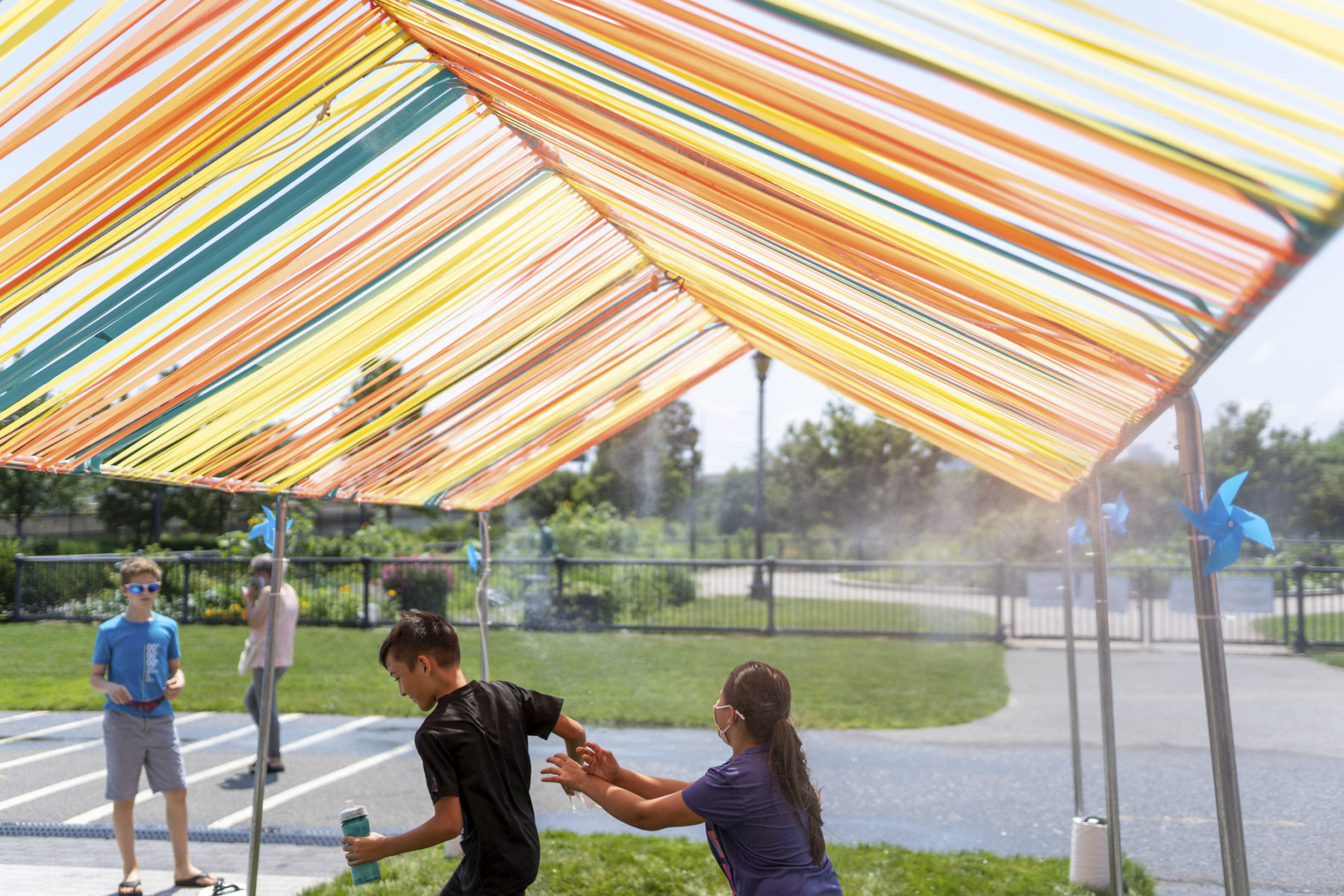 Children playing under the shade structure while it releases cooling mist