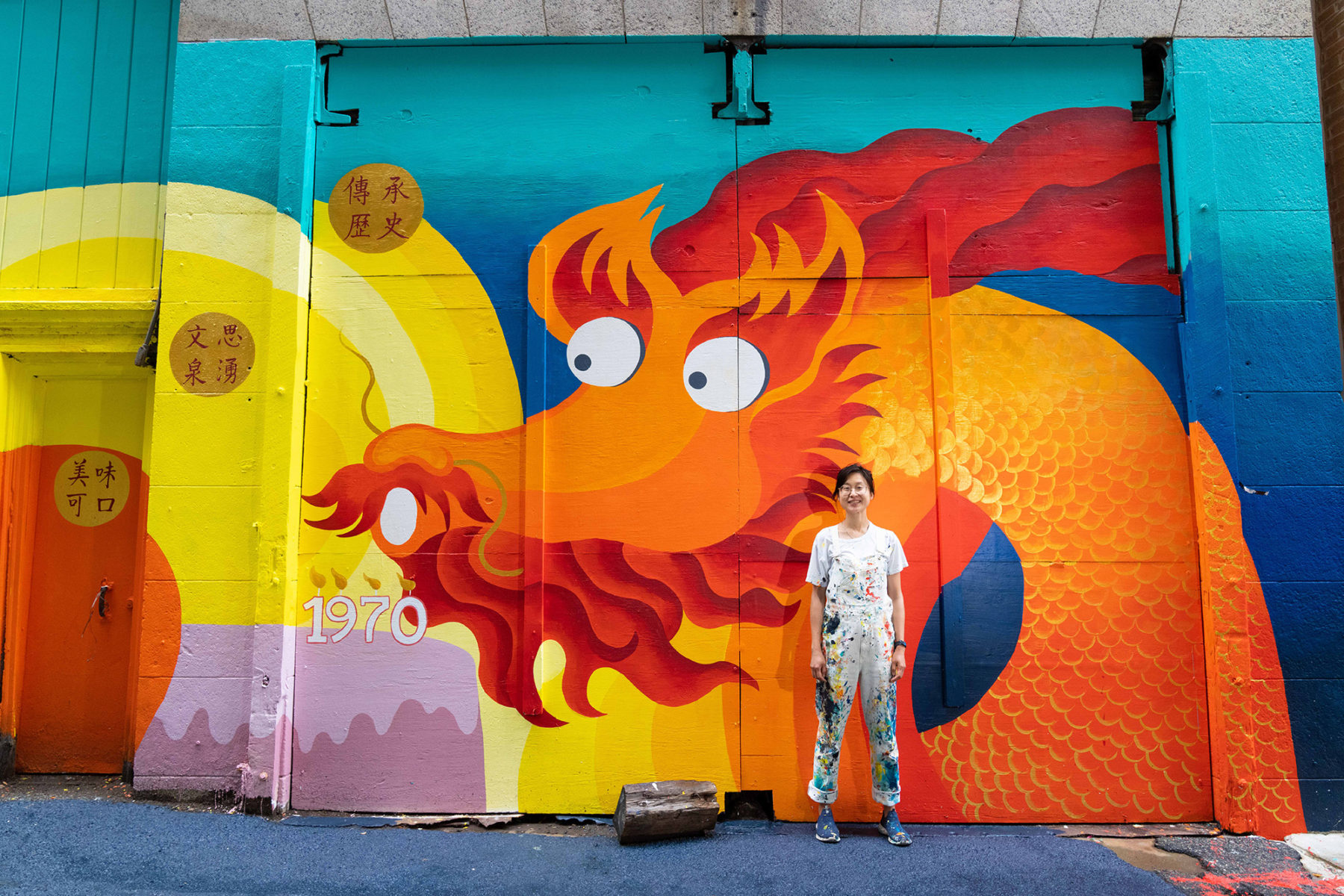 Artist stands in front of brightly colored mural in Chinatown
