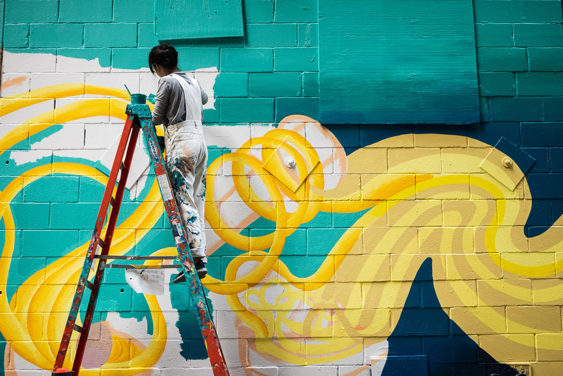 Artist on ladder fills in white space on mural