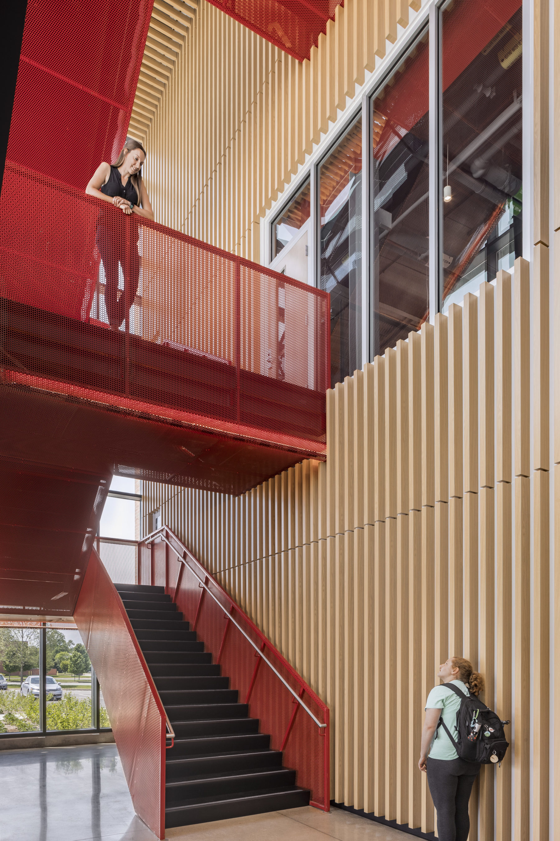 interior photo of red feature stair. One student stands on landing talking to another a floor below.