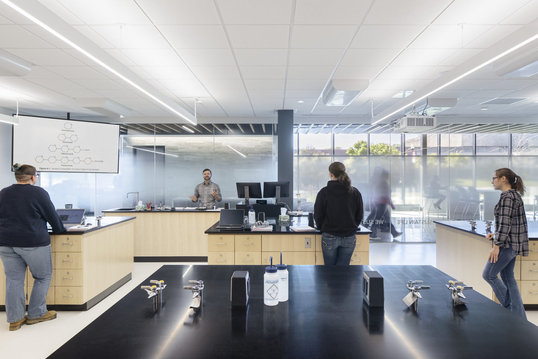 interior photo of lab space, an instructor stands behind a lab bench speaking to students