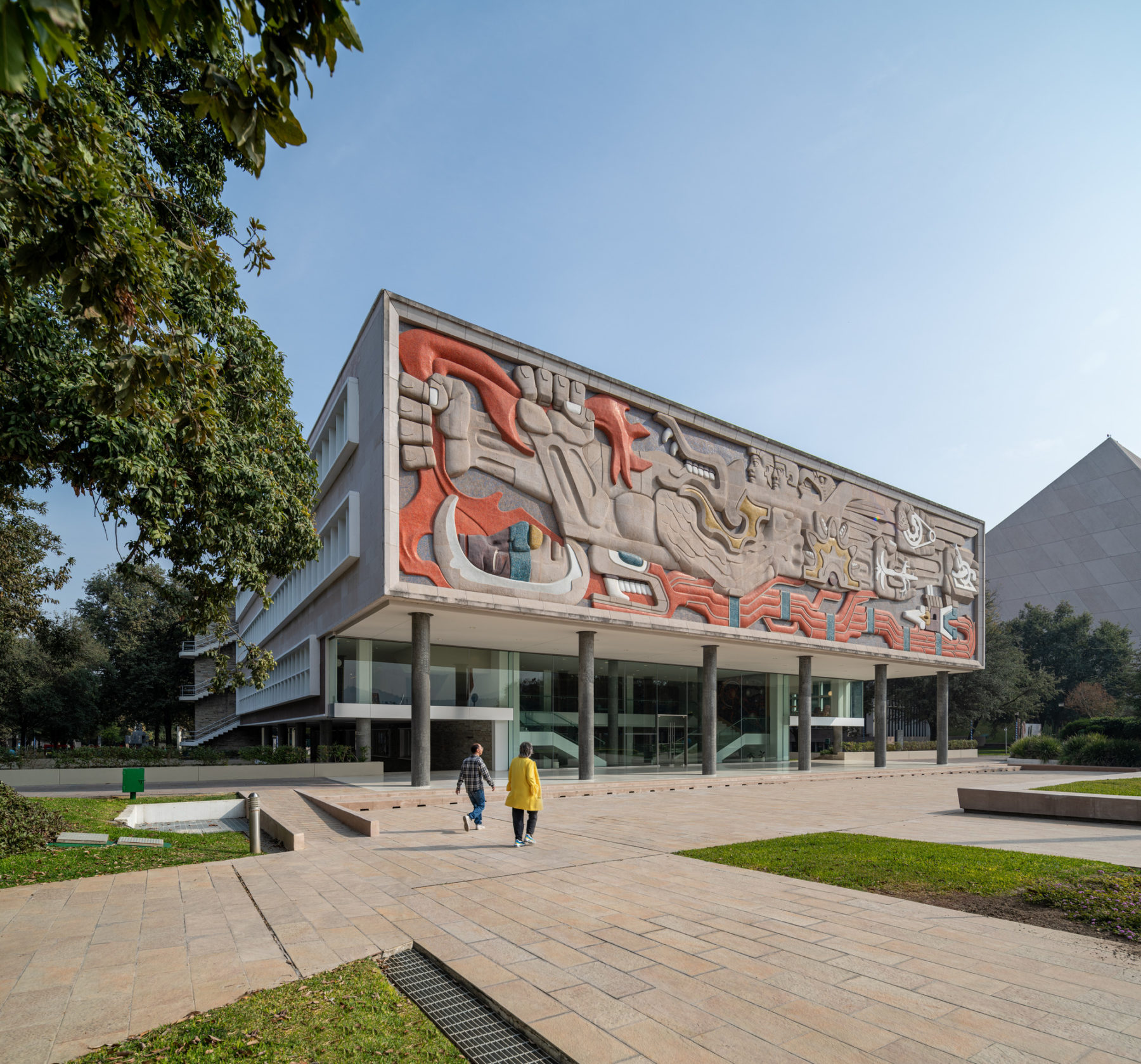 exterior daytime photo of building from an oblique angle. Two people walk in front on the entry plaza.