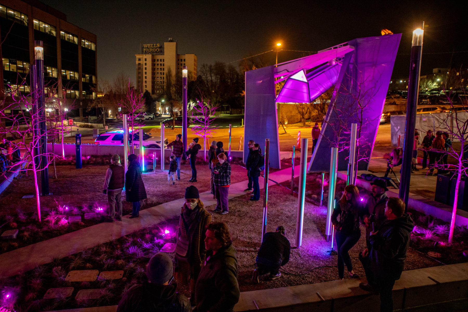 Nighttime picture of architectural sculpture at plaza entryway illuminated in purple