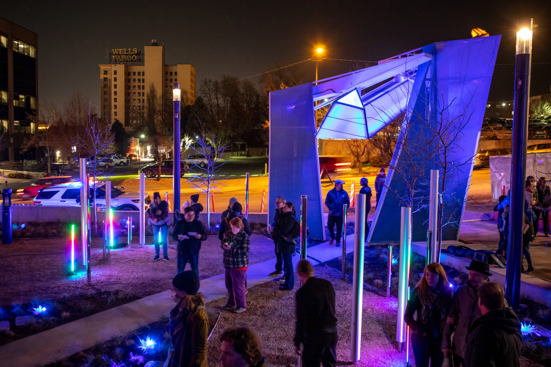 A nighttime view of people walking through the architectural sculpture at the plaza's entry