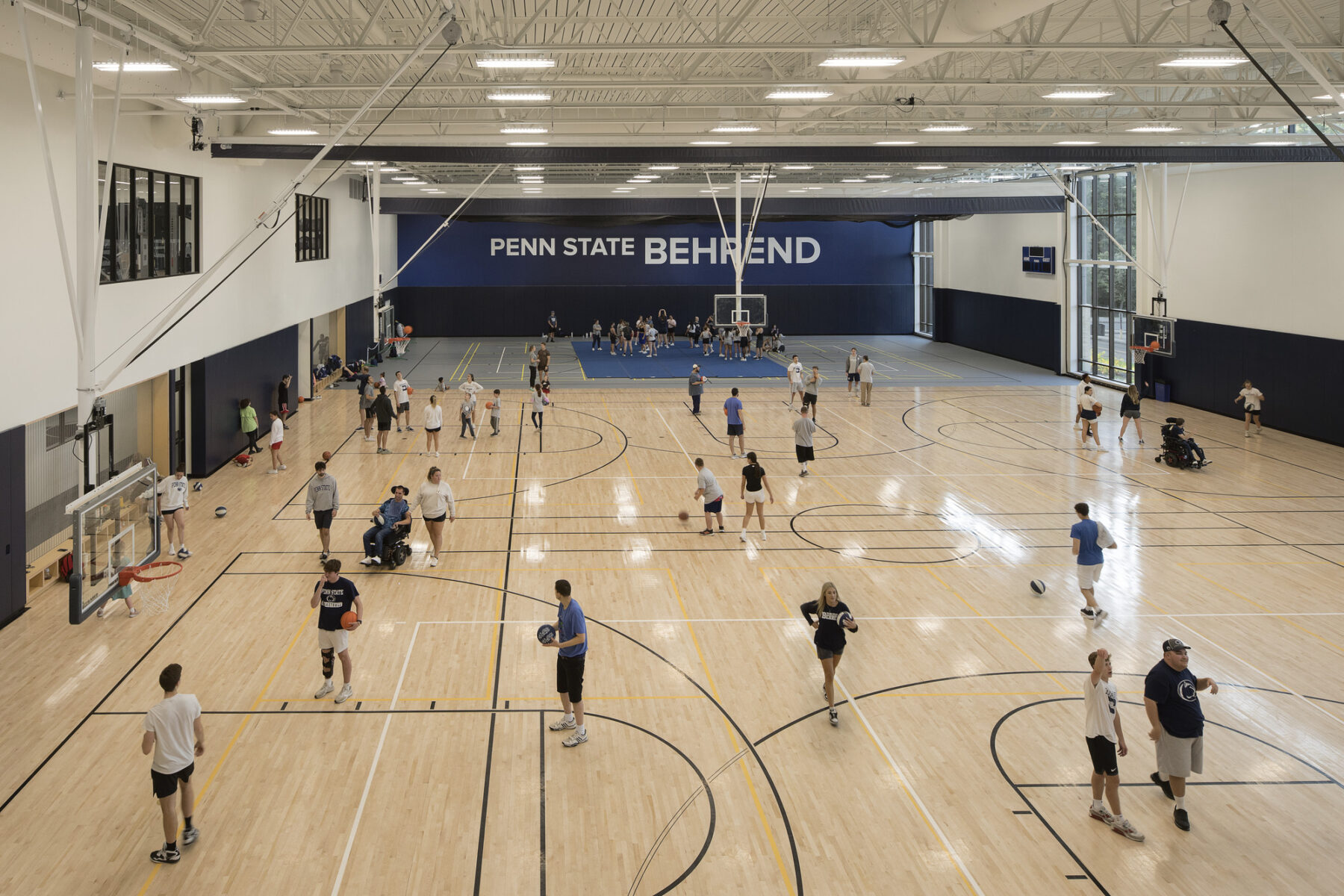elevated interior photograph of large gymnasium space with basketball courts and multi-use courts. Lively with lots of people using the space