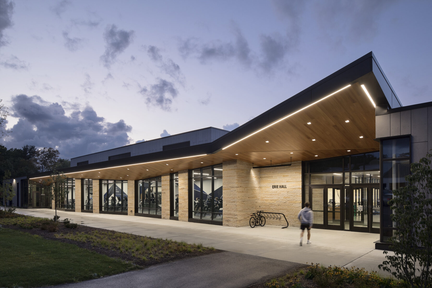 exterior dusk photo of recreation center entry with cantilevered roof overhand and wood ceiling