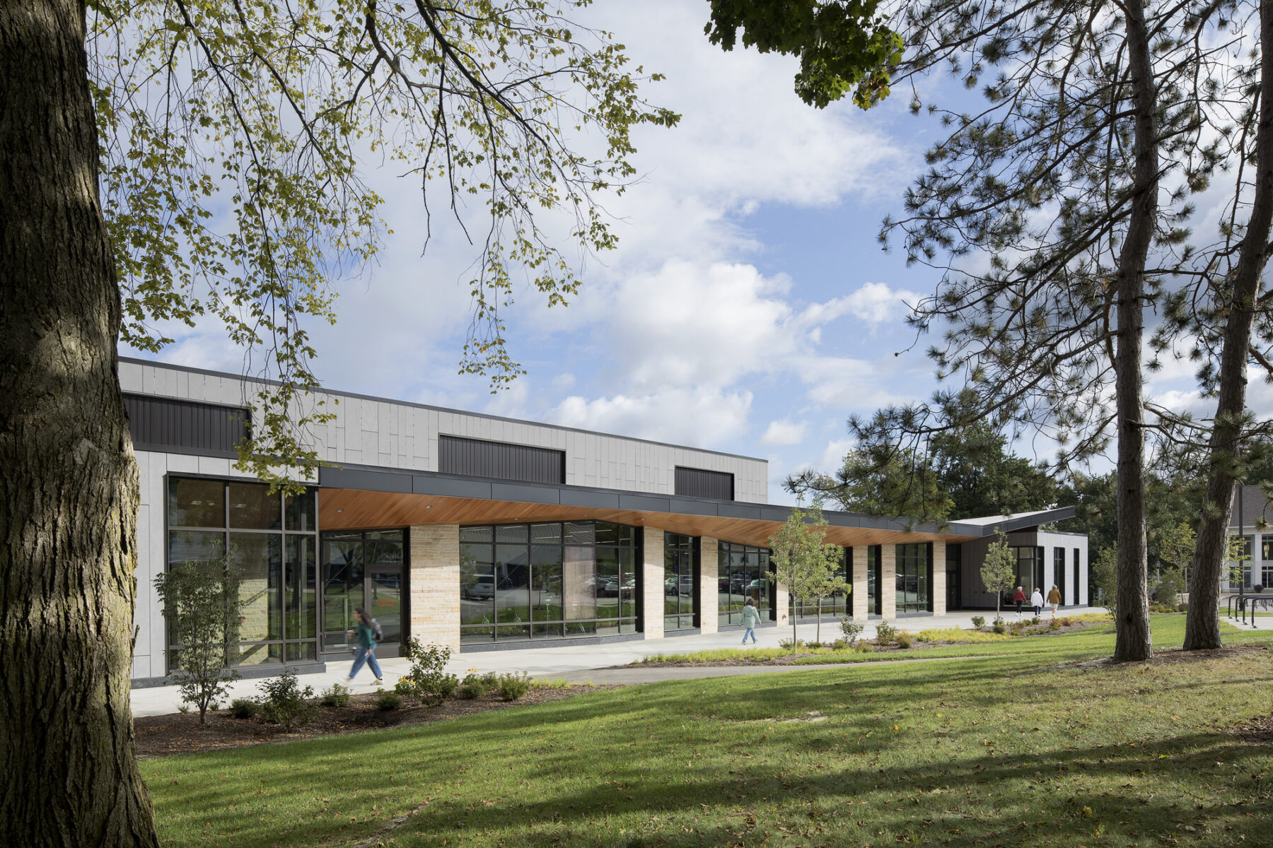 exterior daytime photograph of recreation center, with trees framing the view. People walking by the building