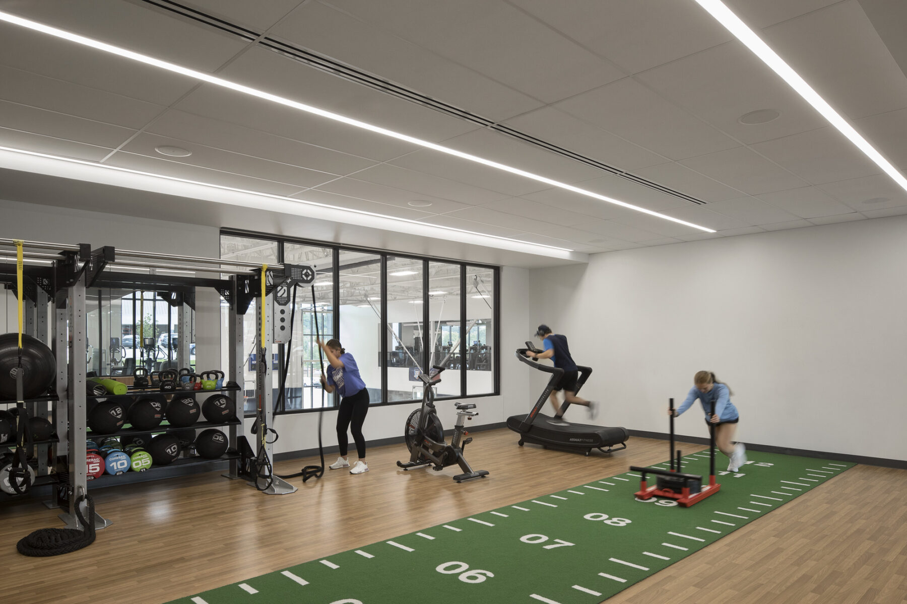 interior photograph of a multi-purpose room with sled pushing, boxing bag, spin machine, and other equipment. Window overlooking gym