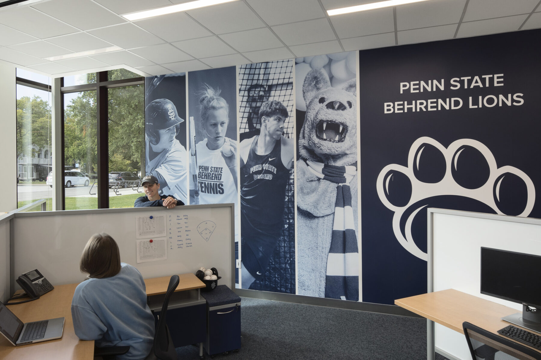 Interior photograph of office space with large wall graphics with athletes and mascot in school's blue colors