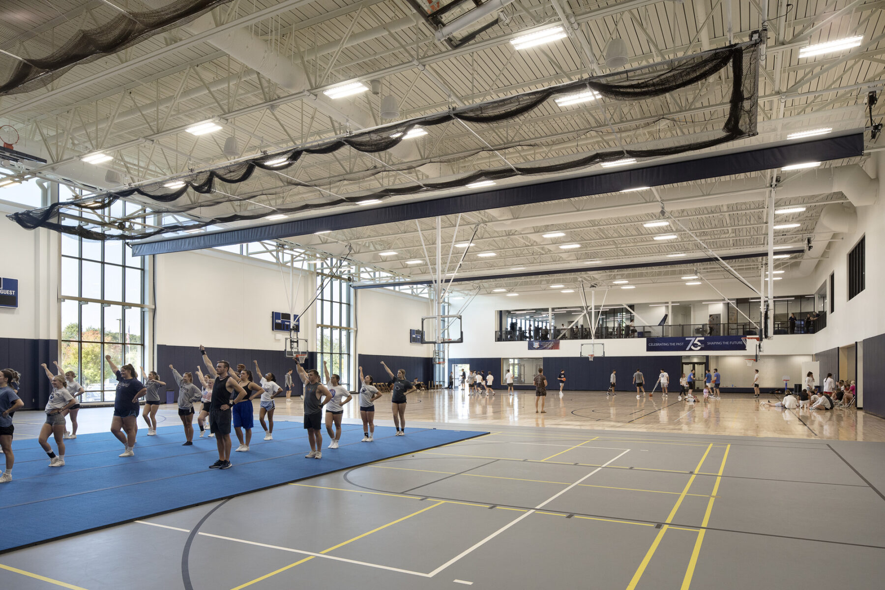 interior photograph of large gymnasium space with basketball courts and multi-use courts. Cheerleaders practicing in foreground