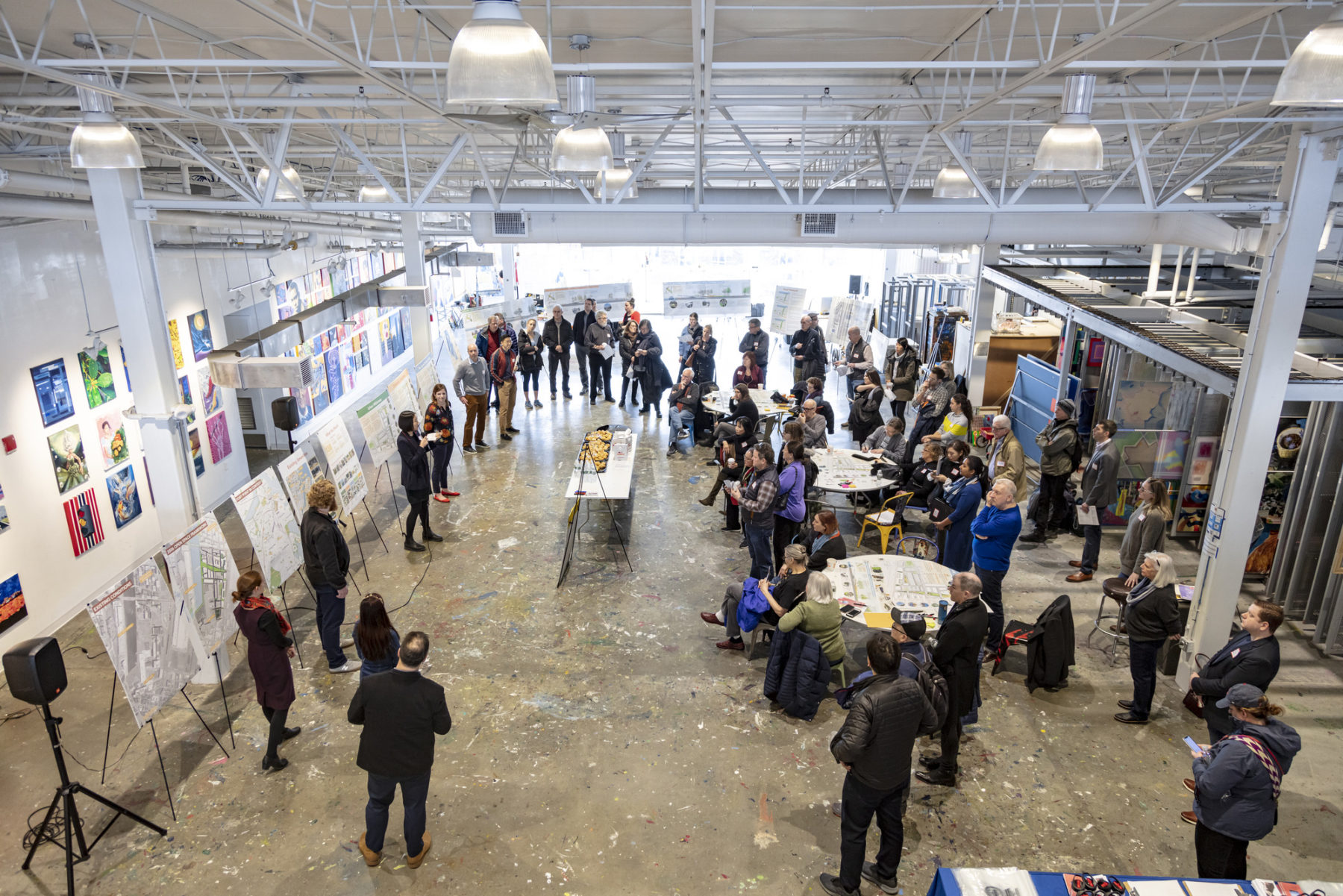 photo of public engagement session taken from balcony above. boards are set up and presenters talk about the project to the crowd