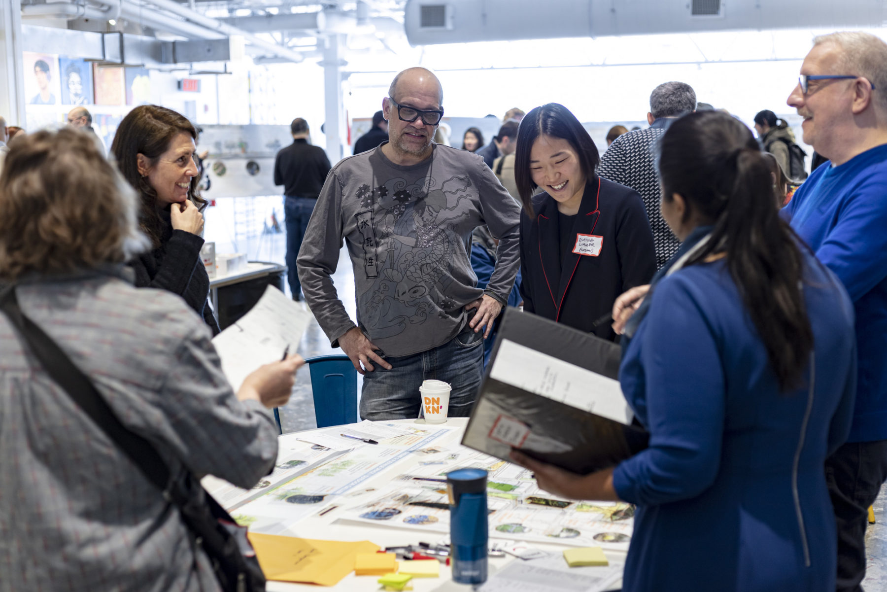 photo of people standing around a table looking at a plan during public engagement session. A woman from the design team discusses potential features.
