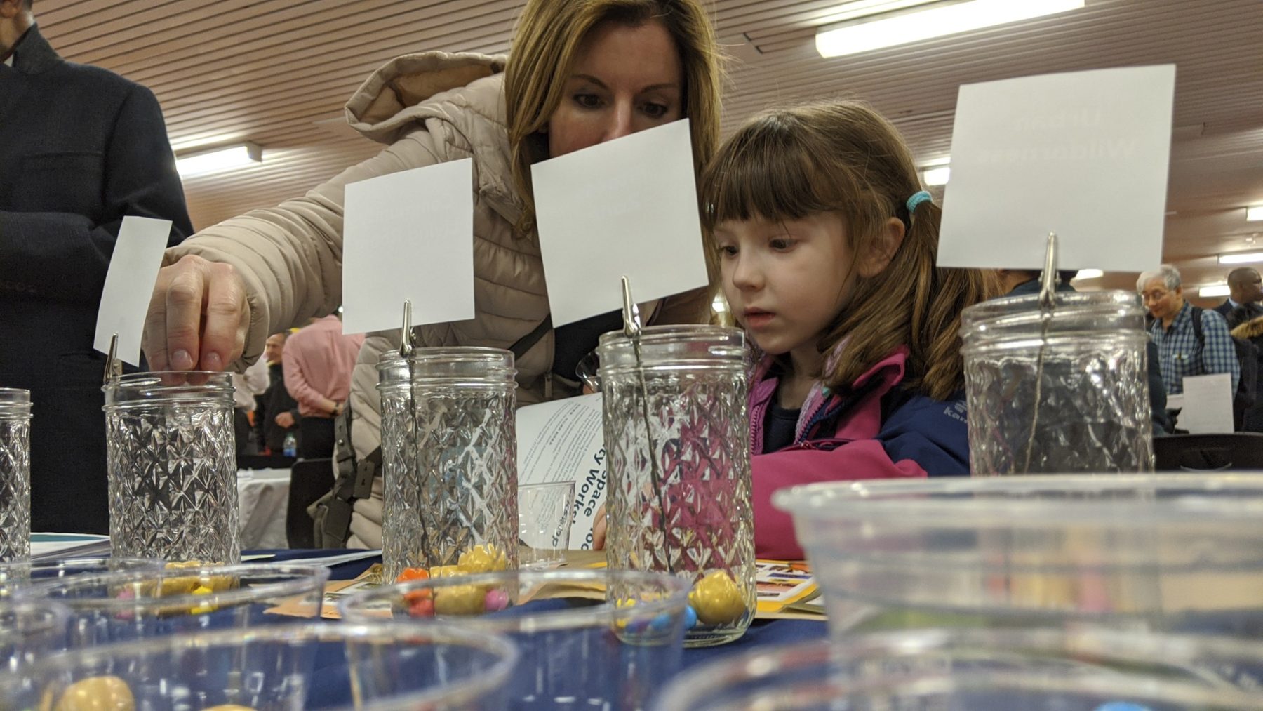 photo from public engagement session. a mother and daughter place small balls in glass jars to vote for favorite park features