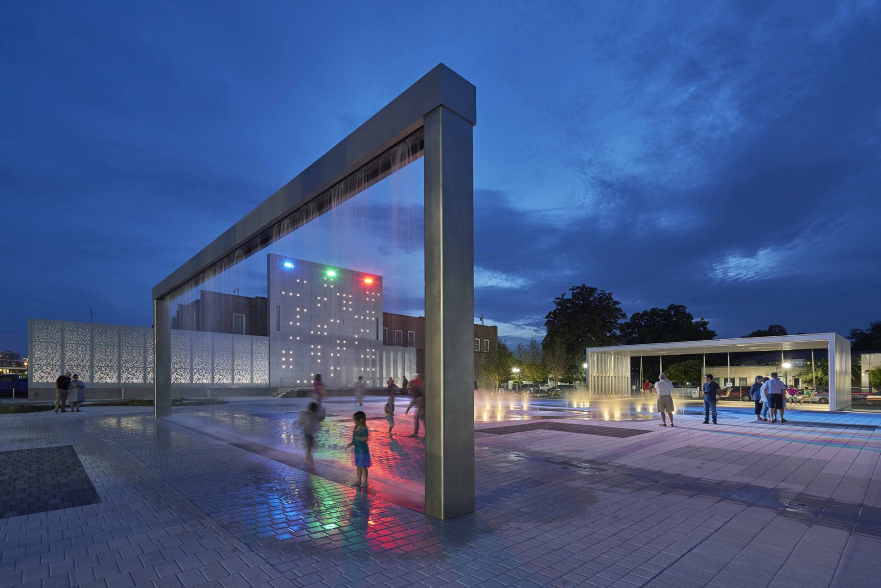 photo of plaza at night kids play under a water feature