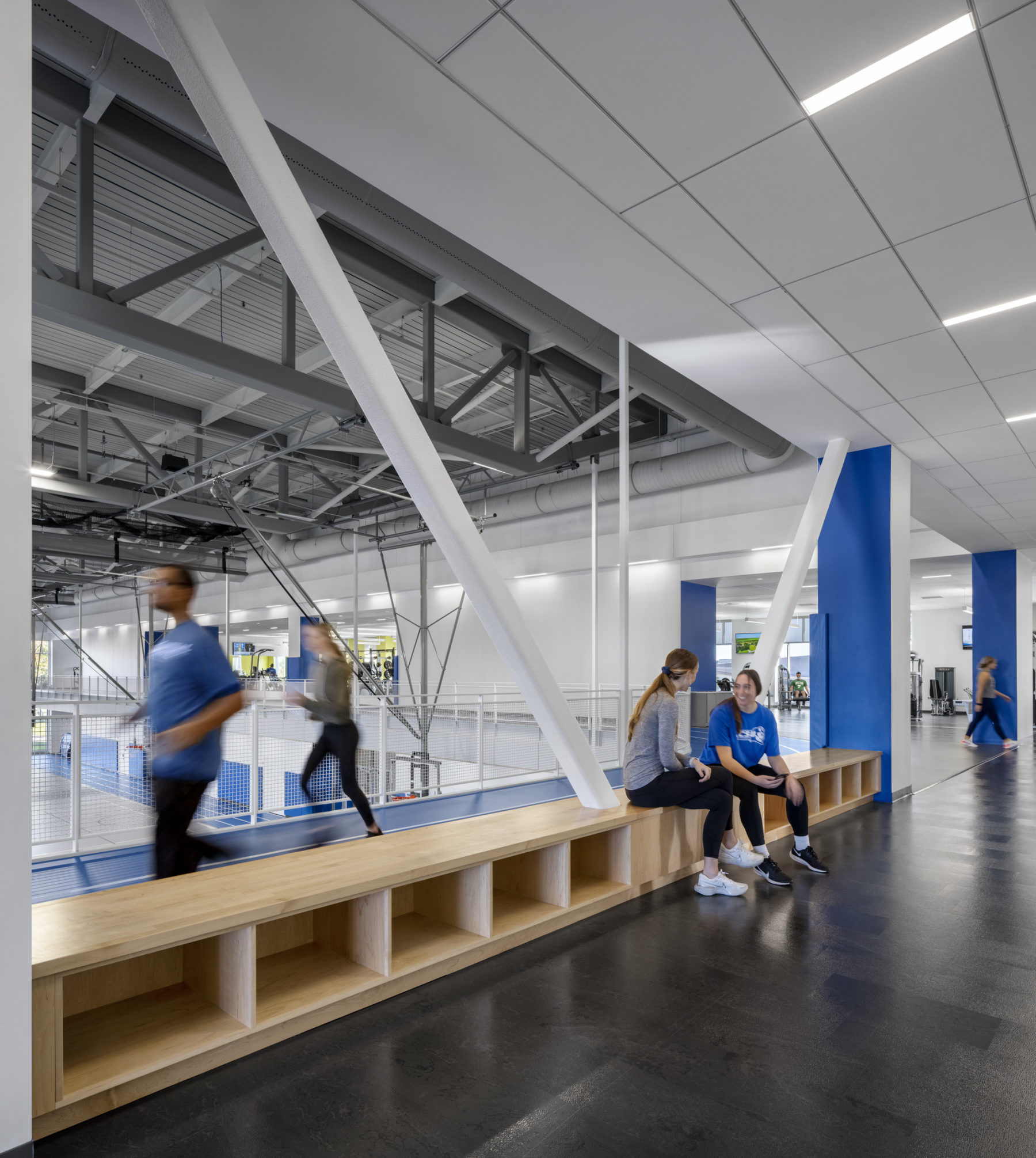 interior photo of bench next to elevated track. two students run on track while two others sit and talk on bench