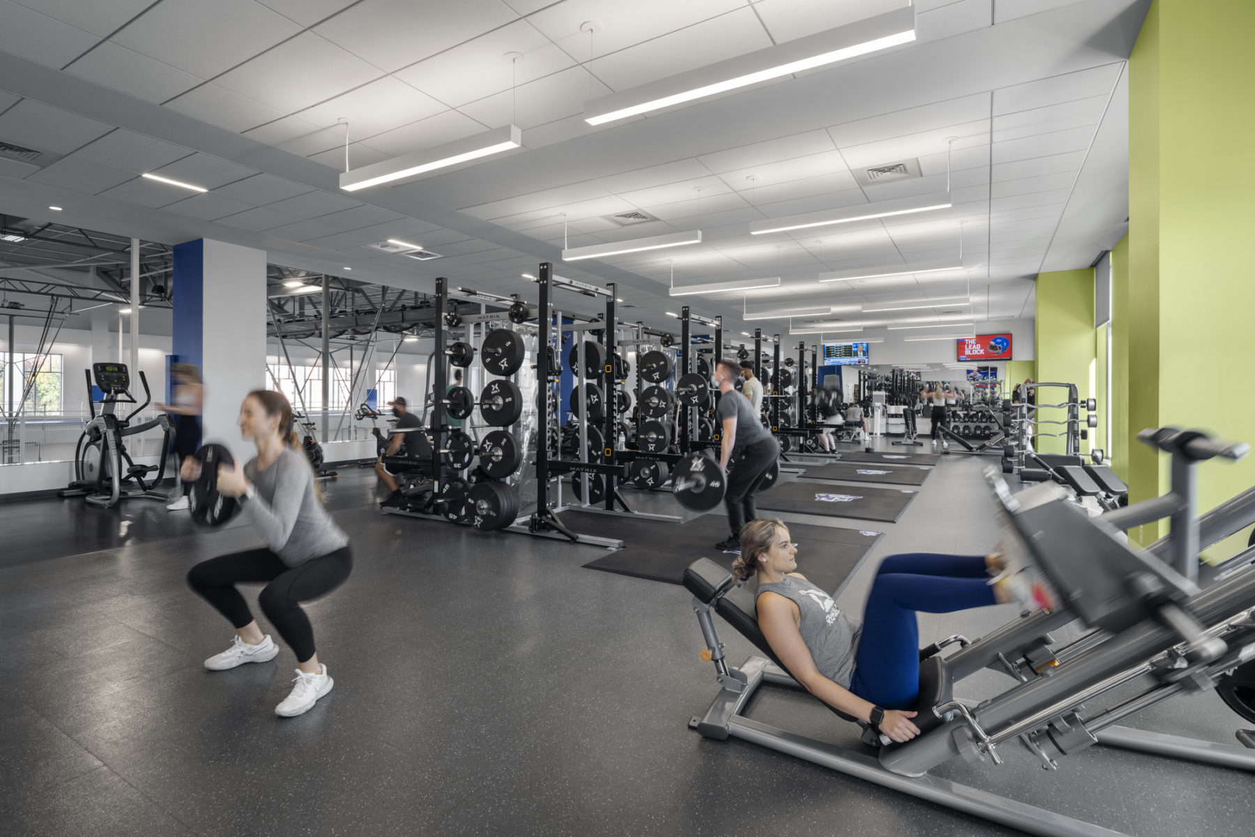 interior photo of weight training zone. a woman squats with a weight in the left foreground
