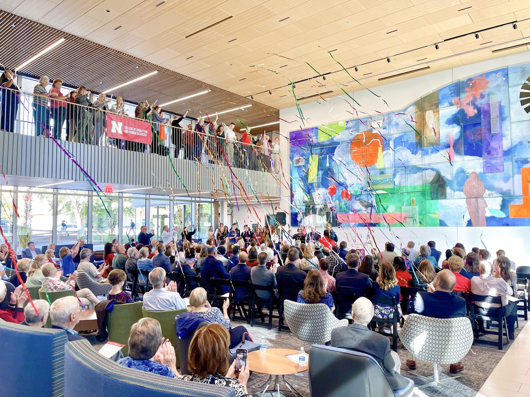 People sitting in double height common space as streamers fly from the ceiling in celebration