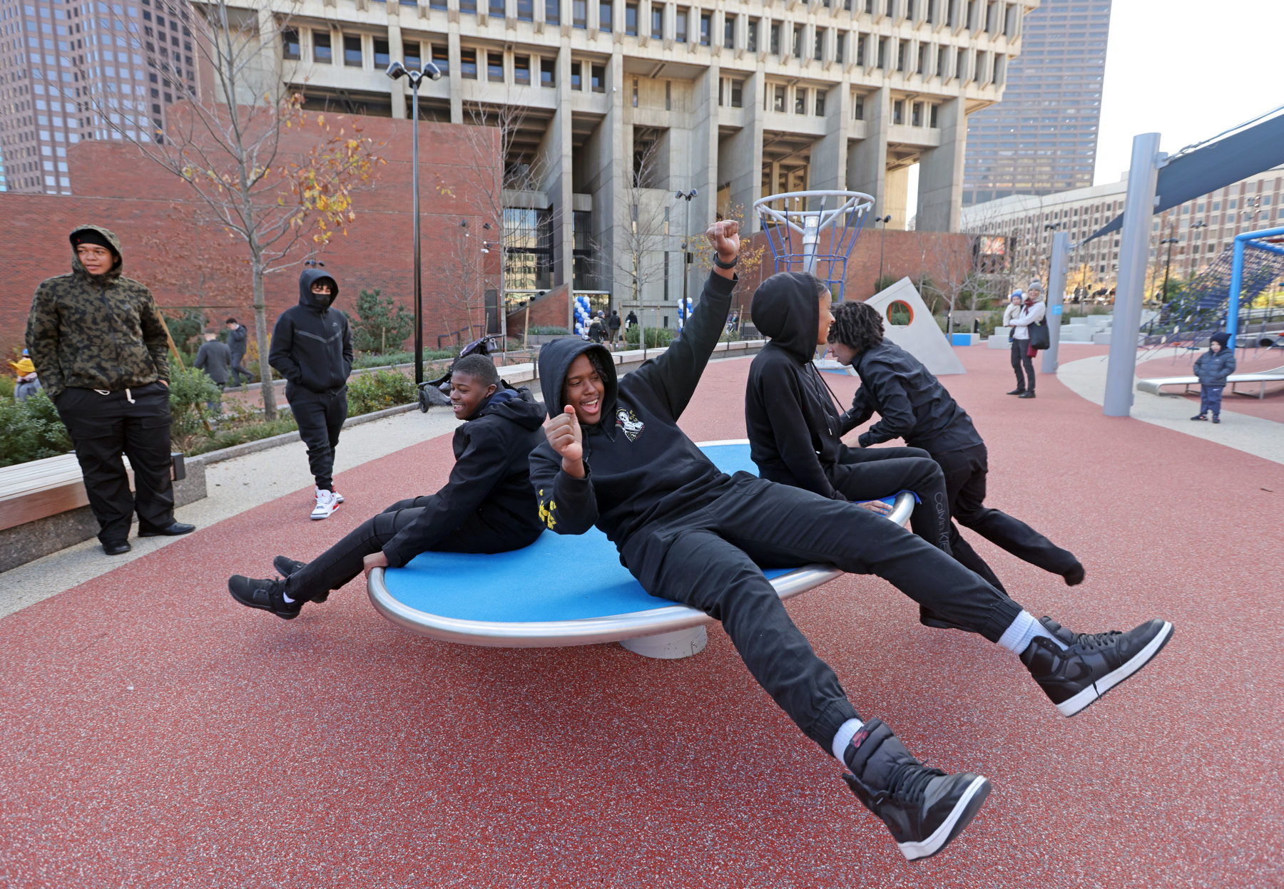 Three older kids spinning around on a play feature in the plaza's new play space