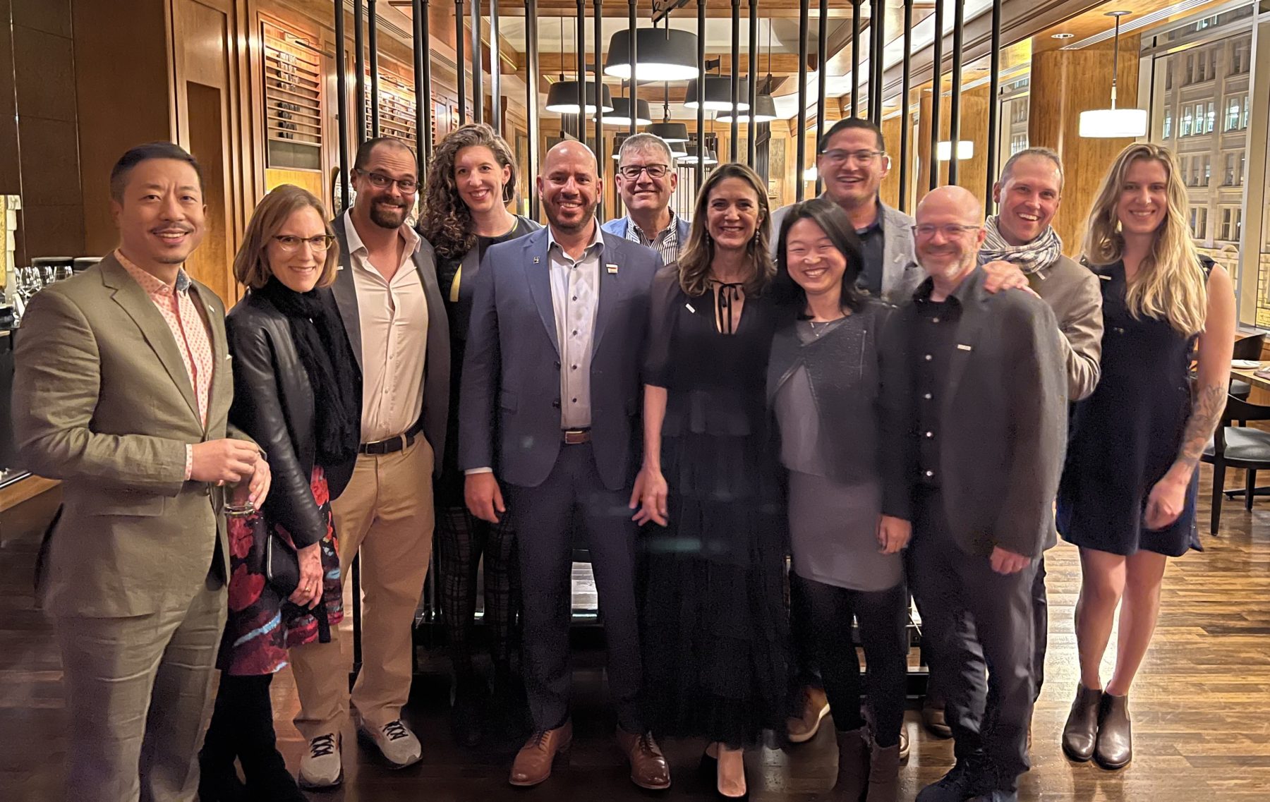 A group of 12 people standing together smiling in a restaurant