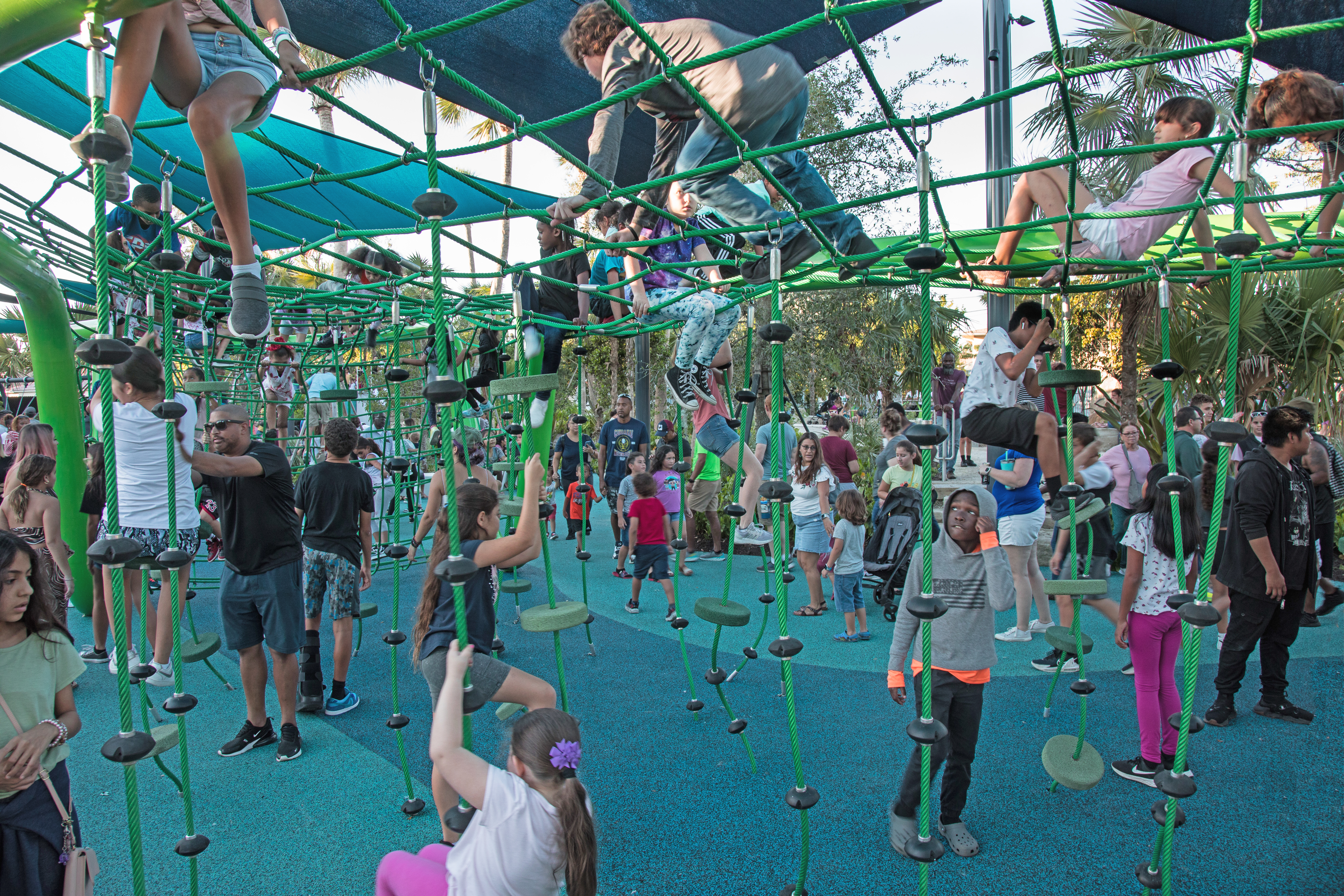 A bunch of children playing on a large play structure with hanging ropes to climb on