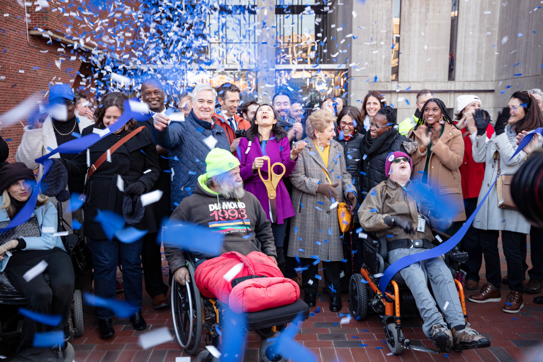 Surrounded by a group of people, Mayor Wu cuts the ribbon and confetti flies all around