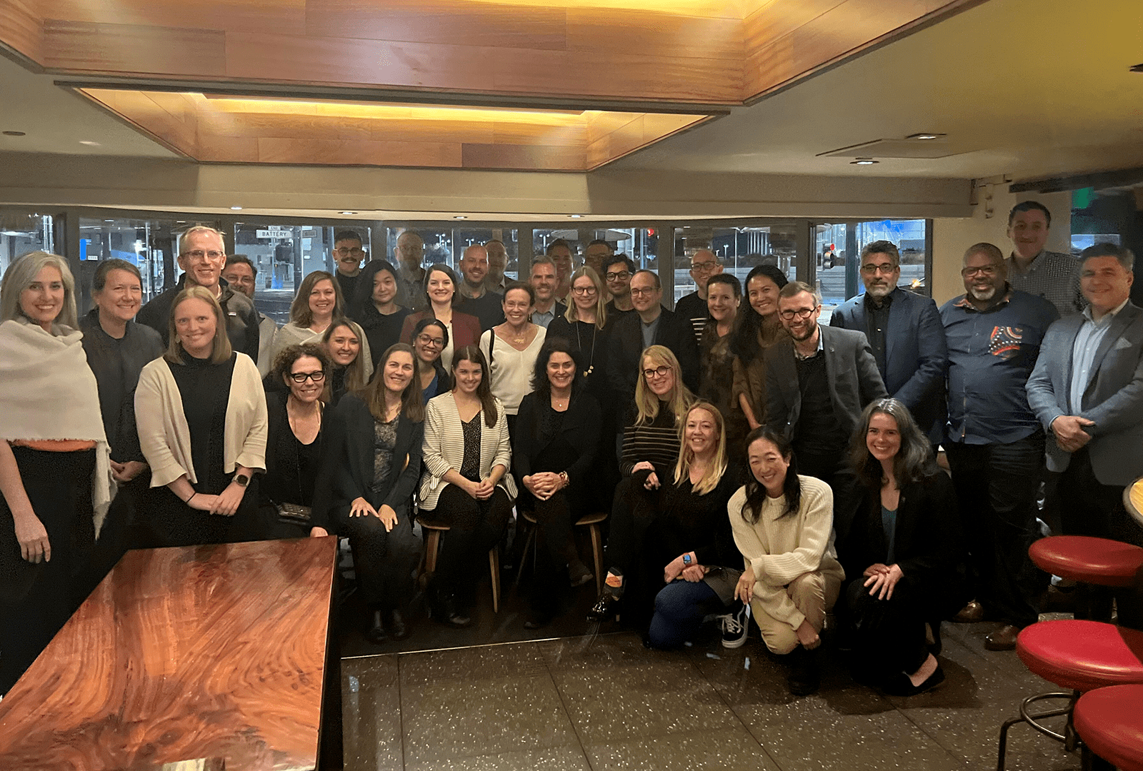 A crowd of 20-30 people gathered, smiling, in a restaurant