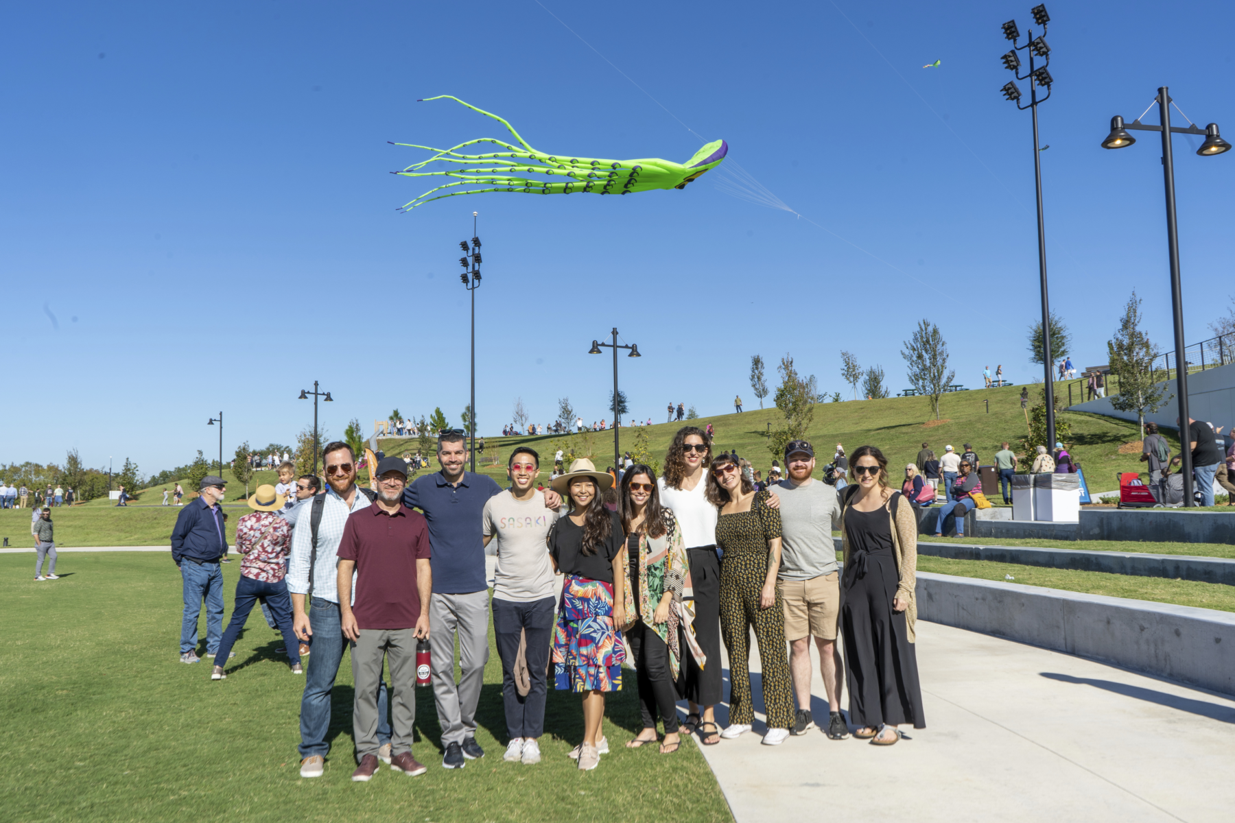 The Sasaki design team posing as a group with a green kite flying against a blue sky behind them