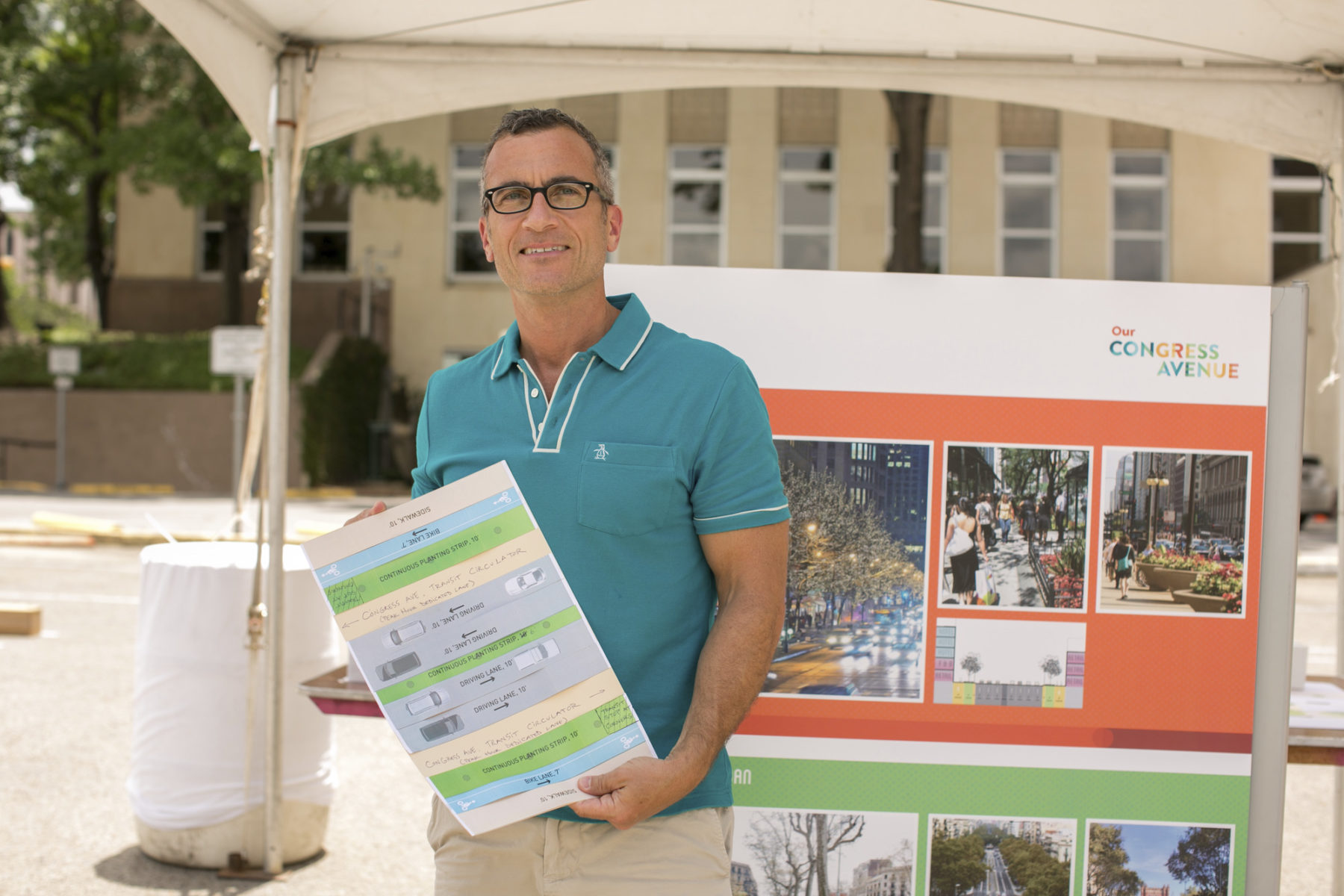 photo of a man with gray hair in a teal polo shirt holding a print out of the proposed lanes for the avenue. He stands in front of a board with inspiration photos that says 