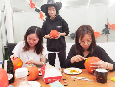 Photo of three people carving pumpkins with Halloween decorations in the background