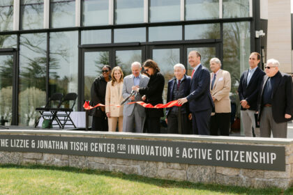 Photo of ribbon cutting ceremony in front of glass facade with a man and woman holding scissors and red ribbon cut in half