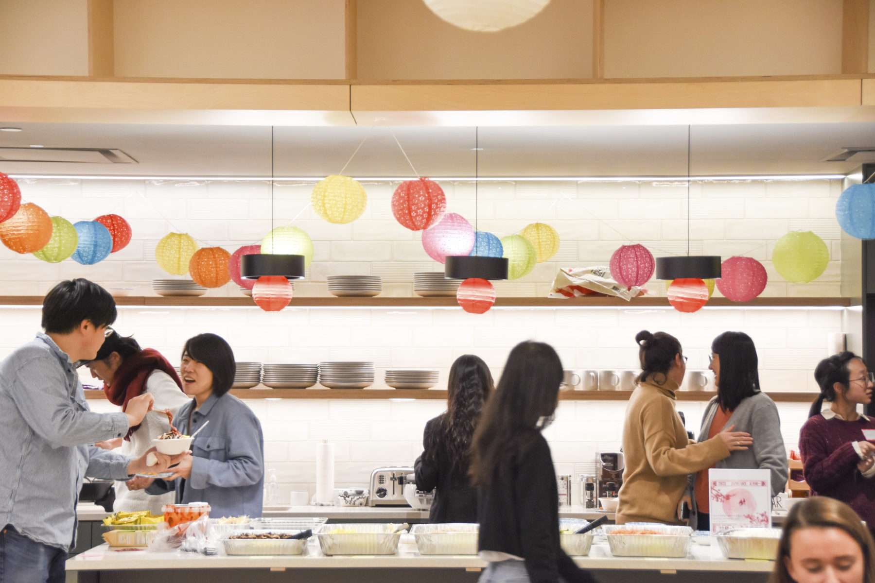 people walking through the kitchen. lanterns hang from the ceiling