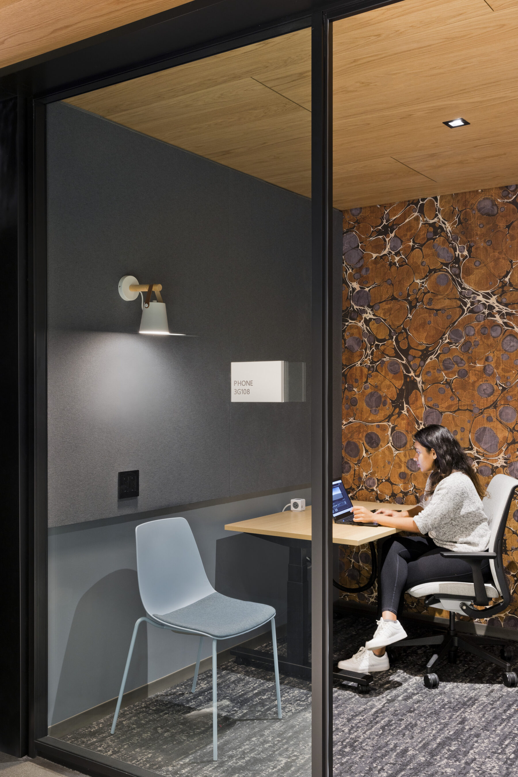 Small enclosed meeting room with floor to ceiling glass doors and single desk with individual working on laptop