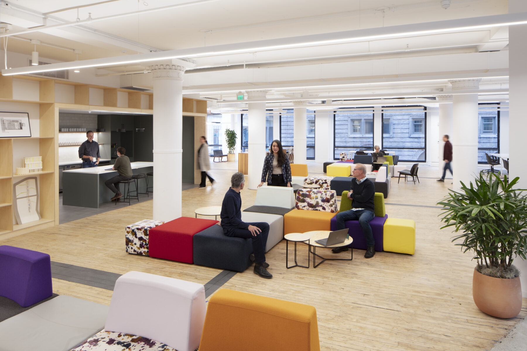 group of people seated on modular furniture conversing with kitchen area in background