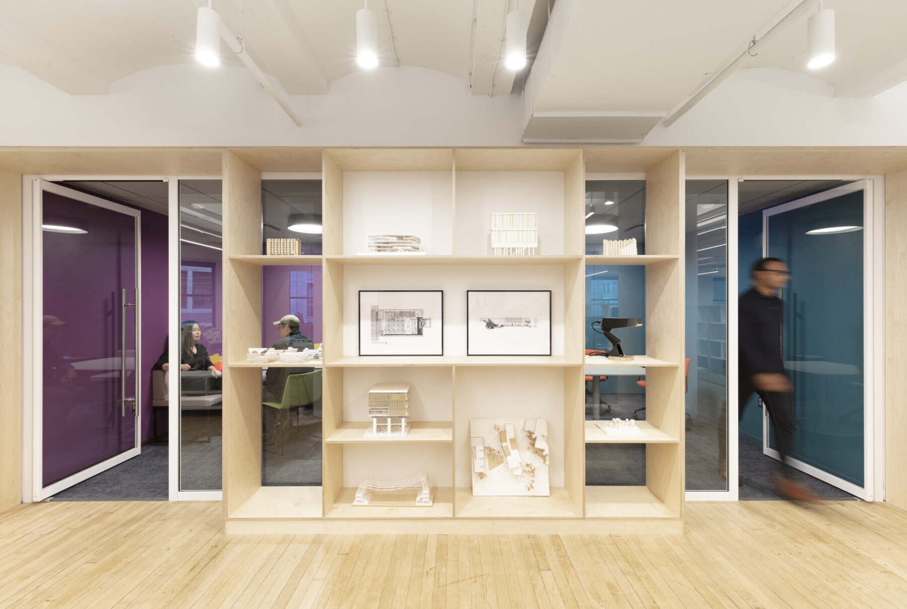 gallery display shelves with architectural models with doors on either side into small, colorful meeting rooms
