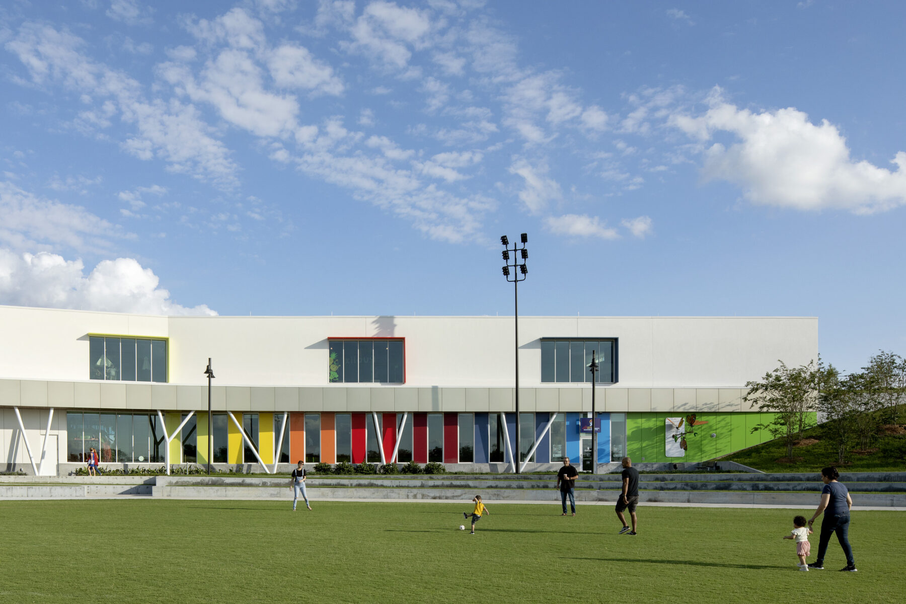 image of Children's Museum with family playing in front lawn, highlighting the pops of color across the facade